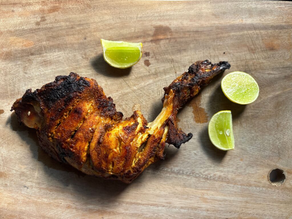 Delicious tandoori chicken leg served with fresh lime slices on a rustic wooden board.