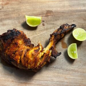 Delicious tandoori chicken leg served with fresh lime slices on a rustic wooden board.